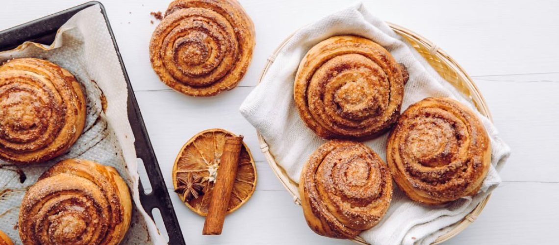 Freshly baked homemade cinnamon rolls in basket and on oven pan in the morning indoors, breakfast concept. Above view.