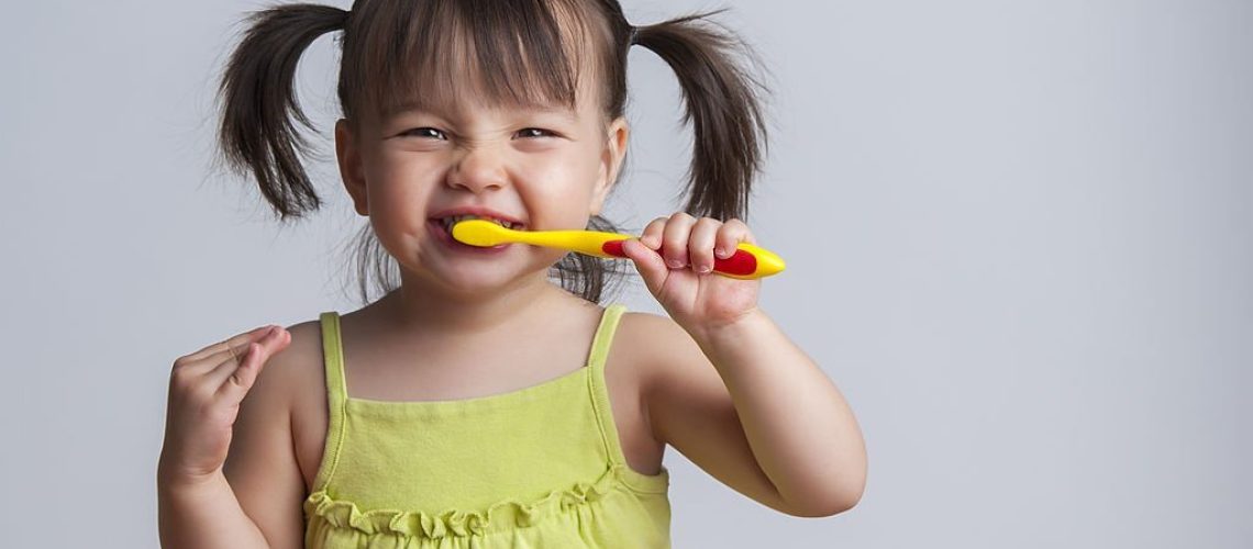 Toddler smiling while brushing her teeth