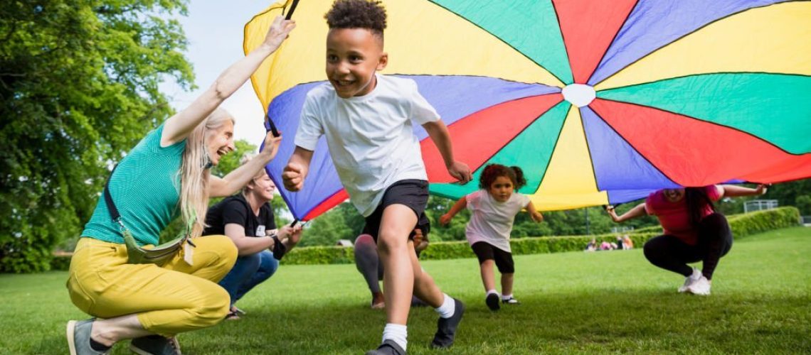 Children playing with a parachute at school during pe in the North East of England. A boy is running underneath it.