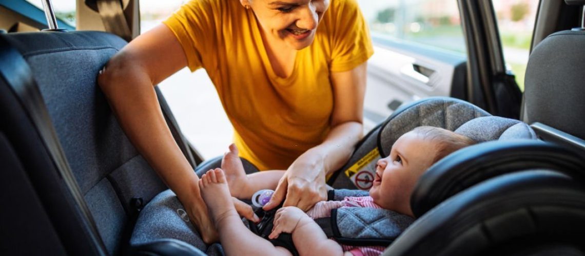 Mid adult mother putting baby girl in car seat