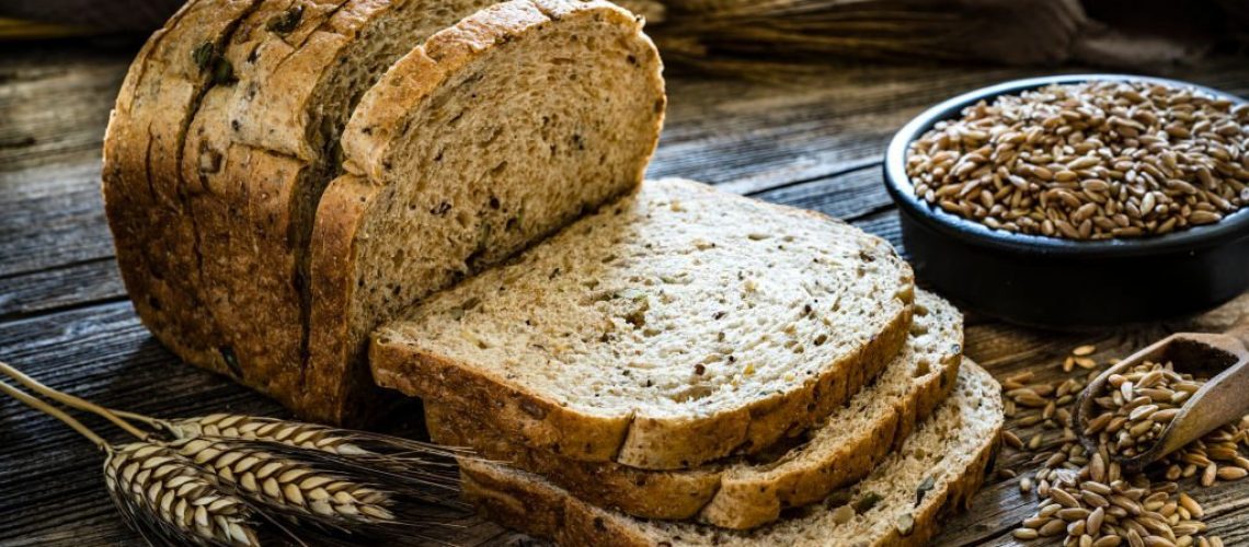 Wholegrain sliced bread shot on rustic wooden table. A bowl filled with wholegrain spelt is at the right beside the sliced bread. XXXL 42Mp studio photo taken with SONY A7rII and Zeiss Batis 40mm F2.0 CF