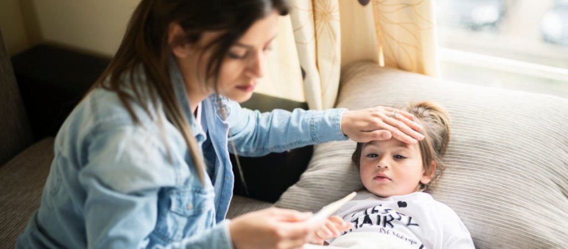 Mother checking temperature on sick daughter laying in bed