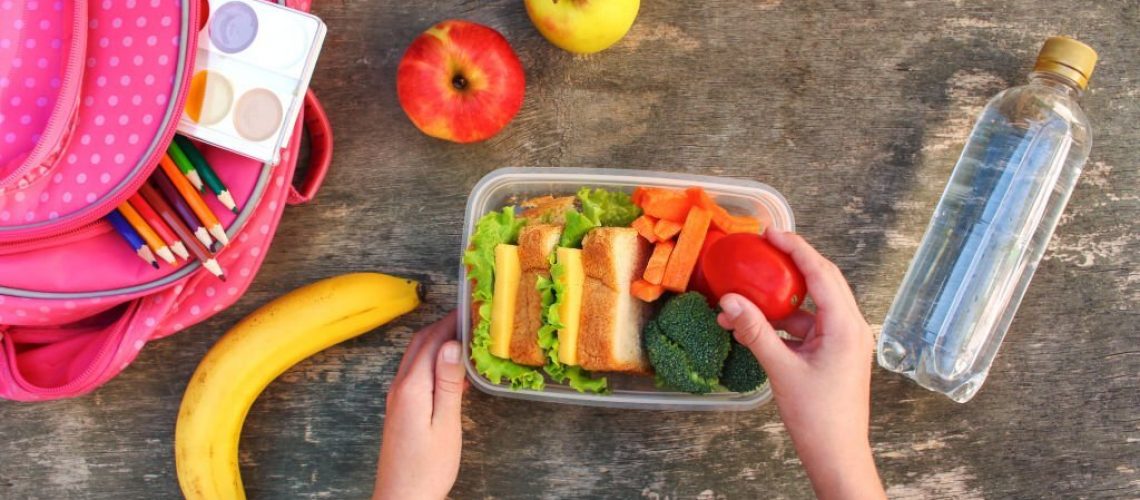 Sandwiches, fruits and vegetables in food box, backpack on old wooden background. Concept of child eating at school. Top view. Flat lay.